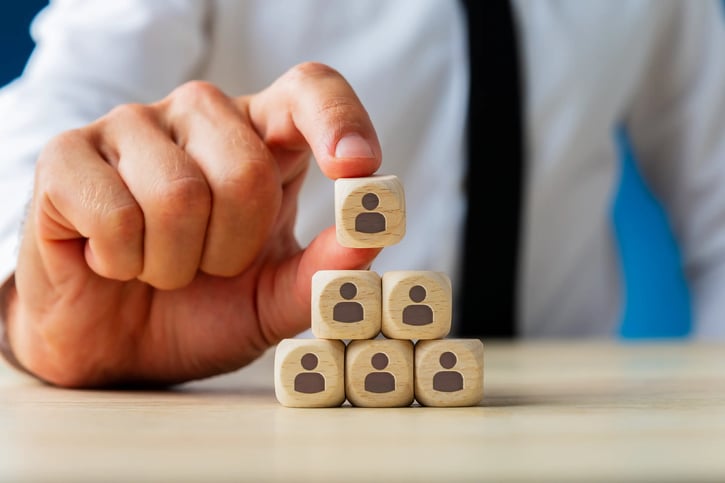 In der Abbildung ist ein organigramm dargestellt, das die strukturierte Organisation eines Unternehmens zeigt, einschließlich der verschiedenen Abteilungen und Hierarchien, die in einem Meeting präsentiert werden. Die Grafik enthält Kästchen und Linien, die die Beziehungen zwischen den Organisationseinheiten und deren Funktionen verdeutlichen.