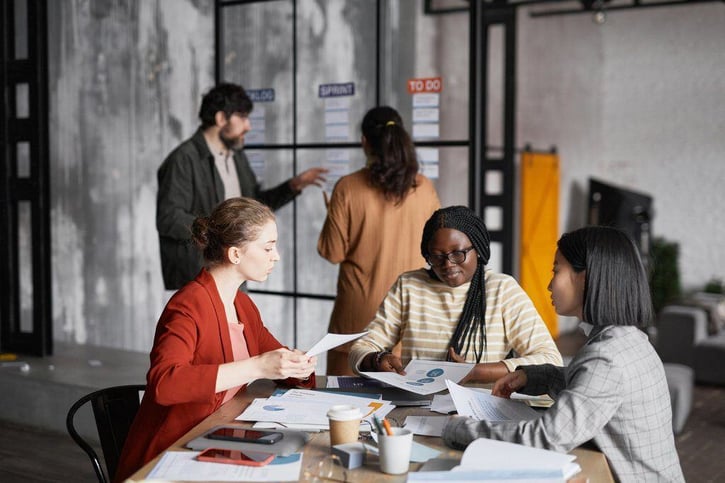 Das Bild zeigt eine symbolische Darstellung des Urteils des EuGH zur Vertrauensarbeitszeit, das die Rechte von Arbeitgebern und Arbeitnehmern bezüglich der Arbeitszeiterfassung und der Flexibilität der Arbeitszeiten thematisiert. Im Vordergrund sind Mitarbeiter zu sehen, die eigenverantwortlich ihre Aufgaben erledigen, während sie die Vorgaben des Arbeitszeitgesetzes in einem modernen Unternehmensumfeld einhalten.